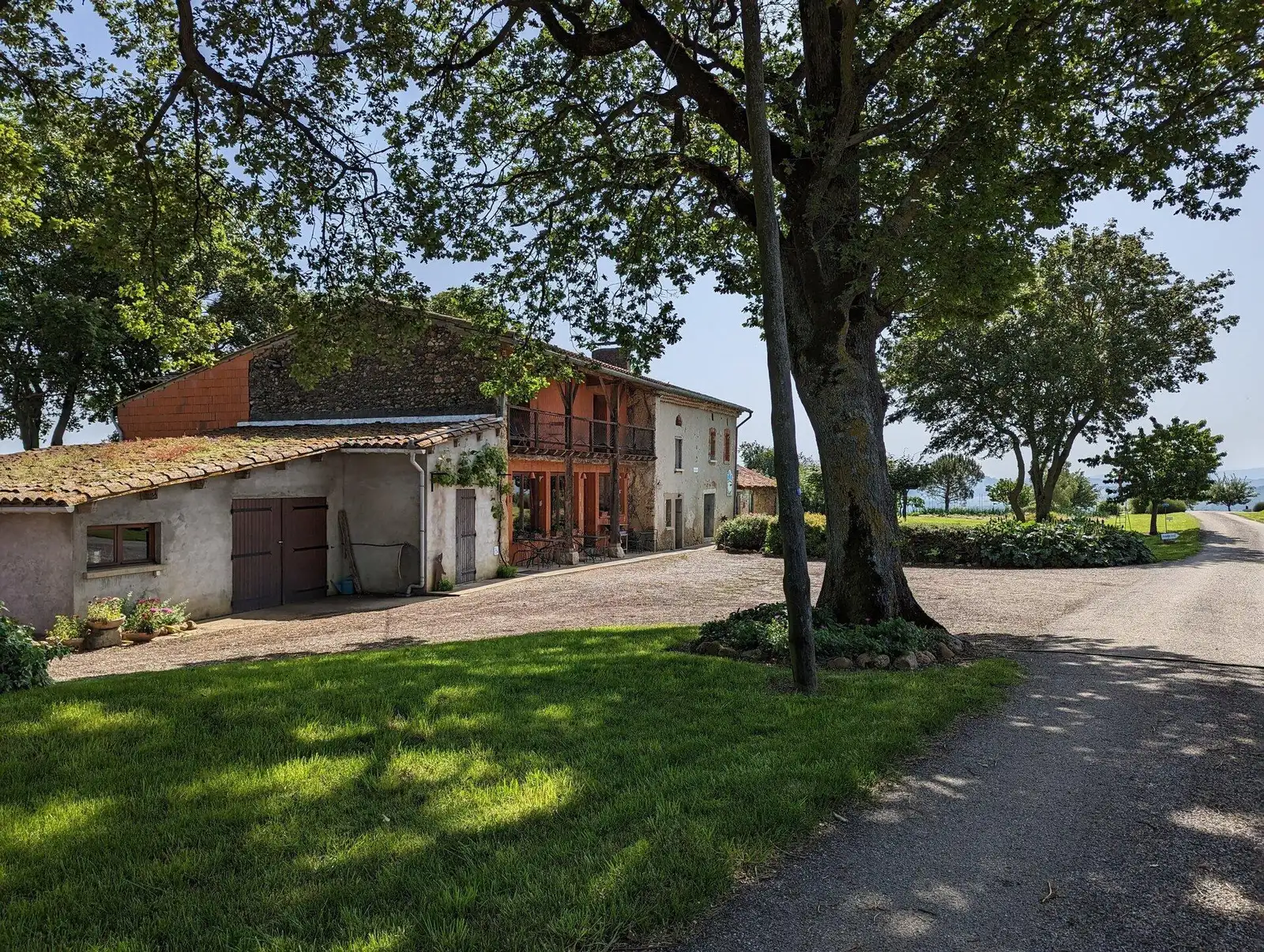 La ferme auberge du Bascou, cour et bâtiment en pierre sous un grand chêne